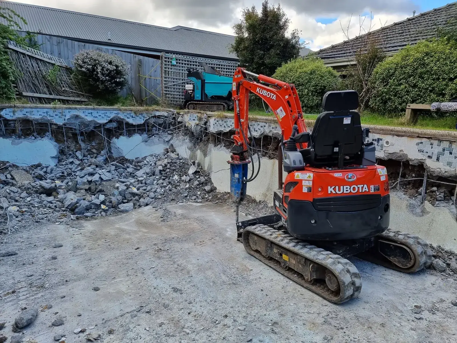 Mini excavator with a rock breaker demolishing a concrete pool