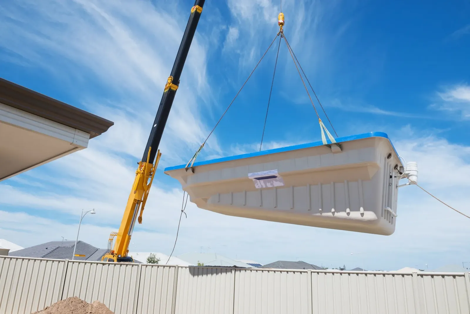 Crane lifting a fibreglass pool shell out of a backyard