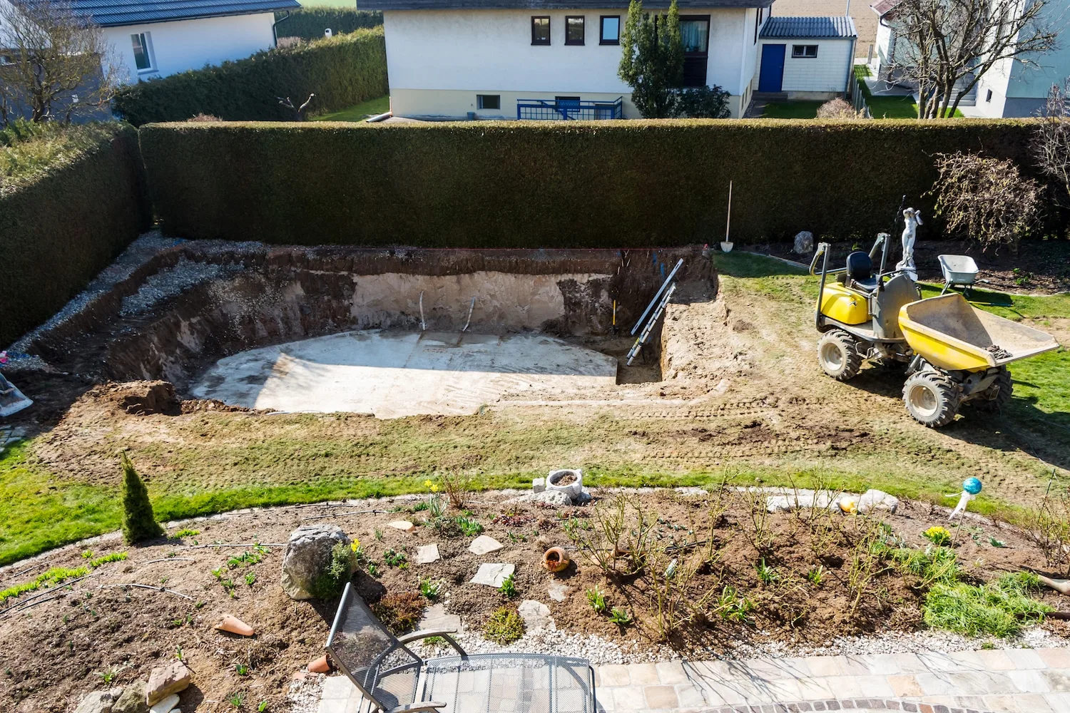 Excavated in-ground pool site with a mini dumper in a fenced backyard
